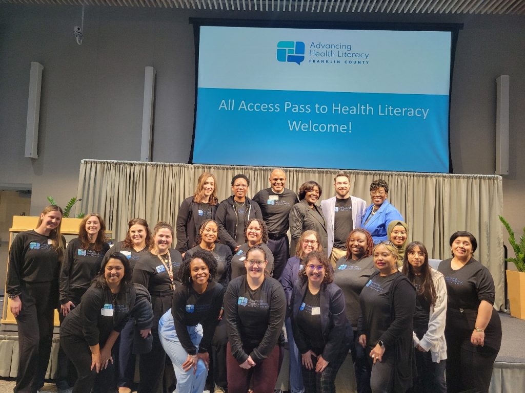 Photo of a group of people wearing matching "Advancing Health Literacy Franklin County" shirts, standing in front of a presentation that says "All Access Pass to Health Literacy: Welcome!"